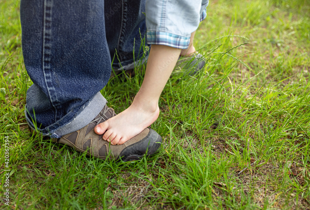 Boy is happy with his first steps supported by his father on a summer meadow. The legs of the child boy stand on the feet of the father, dad supports the little son. Adorable feet on floor at nature. Boy is happy with his first steps supported by his father on a summer meadow. The legs of the child boy stand on the feet of the father, dad supports the little son. Adorable feet on floor at nature.