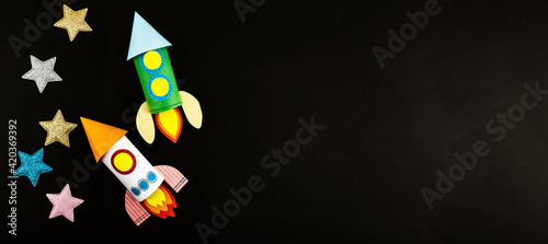 Banner two space rockets made of colored paper on a black background with colored stars. The concept of crafts by the day of April 12 human space flight.