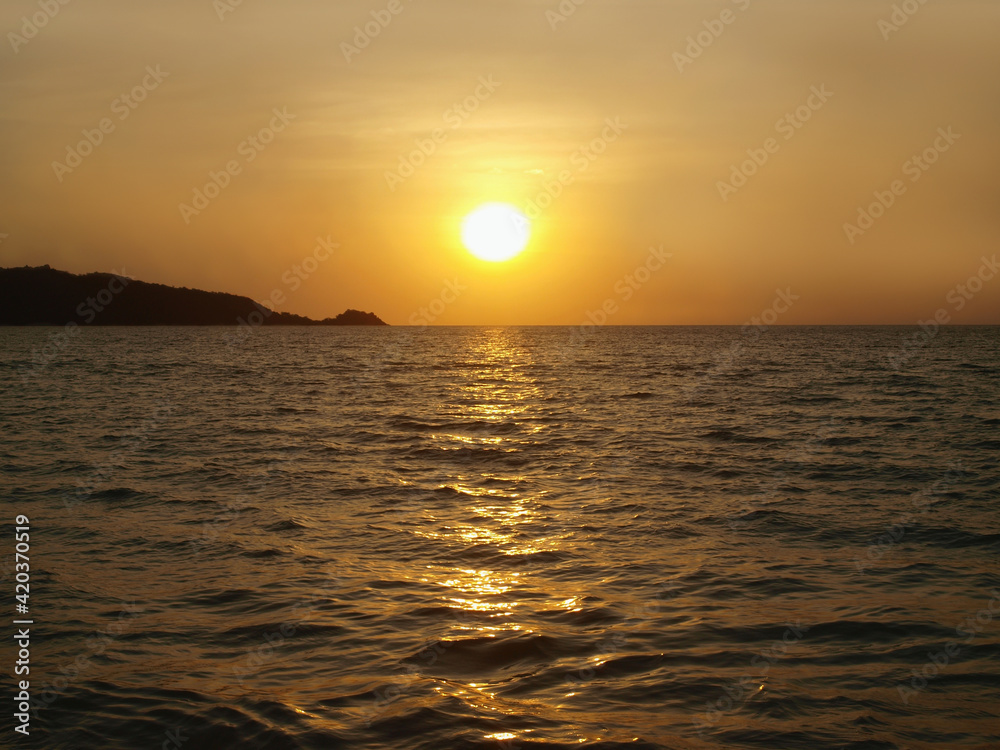 Sunset on the sea. Panoramic view from the coast. Yellow orange sun moving over the horizon. Calm water and dark cape. Orange glow of sundown, sun flare on the surface. Evening on a resort. Ocean view