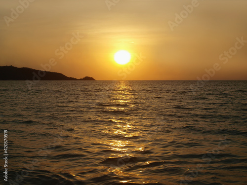 Sunset on the sea. Panoramic view from the coast. Yellow orange sun moving over the horizon. Calm water and dark cape. Orange glow of sundown, sun flare on the surface. Evening on a resort. Ocean view © Oxana
