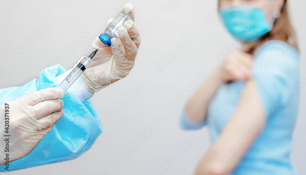 The nurse's hand dials the medicine from the ampoule into medical syringe. A syringe with vaccine in doctor's hand. Injection into the arm of adult. Vaccination concept. The girl in background The nurse's hand dials the medicine from the ampoule into medical syringe. A syringe with vaccine in doctor's hand. Injection into the arm of adult. Vaccination concept. The girl in background