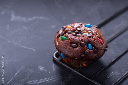 Festive chocolate muffin with colorful sweets. Holiday bun. From above at an angle.