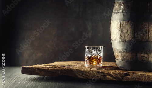 Obraz na plátně Glass of whisky or bourbon in ornamental glass next to a vinatge wooden barrel o