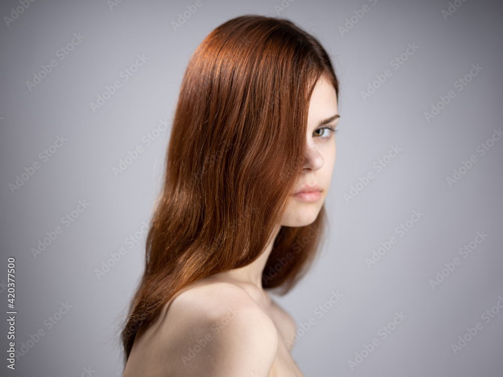 Portrait of a luxurious woman with red hair and bare shoulders on a gray background