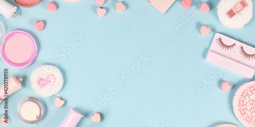 Banner with cute pink makeup beauty products like brushes, powder or lipstick on sides of pastel blue background with empty copy space in middle © Firn