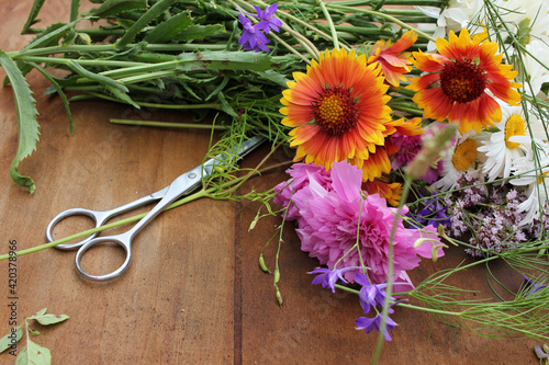 Bunch of flowers and scissors on a wooden table. Making bouquet or midsummer floral wreath process. Farm rustic lifestyle. Top view
