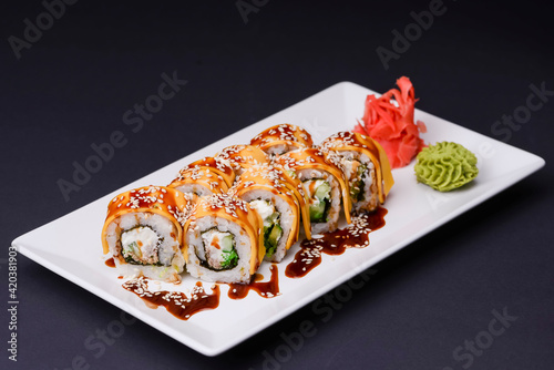 Eel, salmon and tuna sushi with unagi sauce served on a white plate over black background.