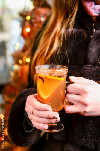 Warm mulled wine in female hands, Christmas decorations on the background.