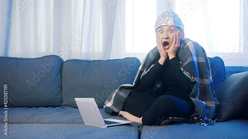 Fearful young woman with aluminum hat browsing social media. Conspiracy theory about 5g network destroying brain. High quality photo