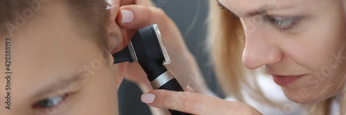Woman otorhinolaryngologist looking at patients ear with otoscope closeup
