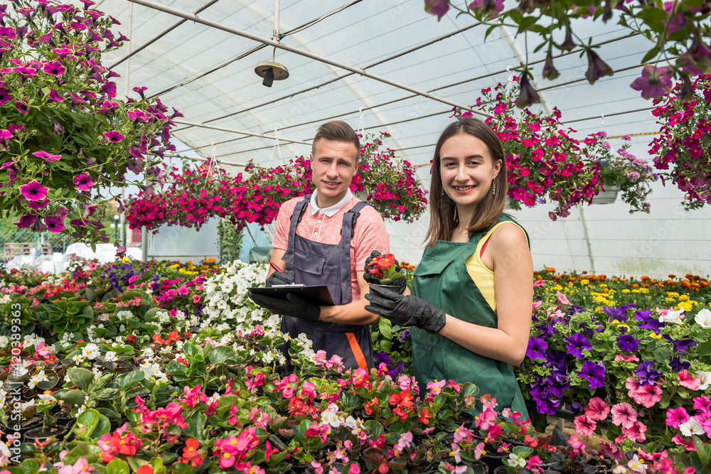 Young male and female florists with clipboard communicating while analzying stock of plants