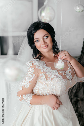 Beautiful sexy brunette bride plus size in a light photo studio. Wedding photo. Plus size model with beautiful makeup and hairstyle. Curvy girl bride with a veil. Wedding bouquet