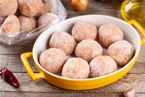 Side view closeup on raw semi-finished frozen meatballs in a baking dish with rice, onion and meat photo