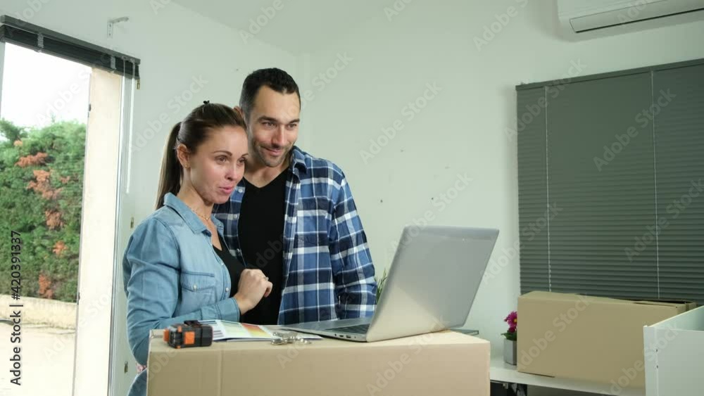 Young couple choosing wall paint color on internet laptop computer for their new house decoration
