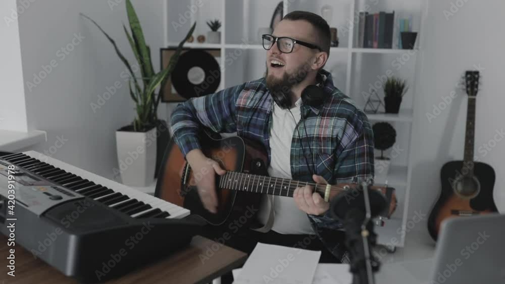 Male musician singing and playing guitar next to his electric keyboard at home Male musician singing and playing guitar next to his electric keyboard at home