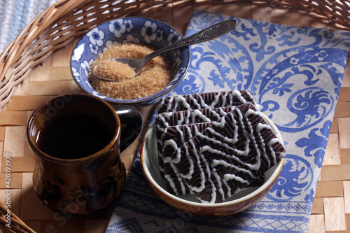 Coffee in a cup, chocolate chip cookies and brown sugar in a blue bowl on a wooden table close-up © yanakoroleva27