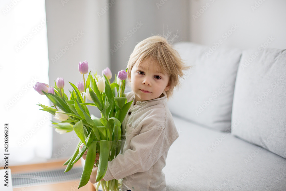Beautiful blond boy, giving mother flowers and box with little gift for mothers day Beautiful blond boy, giving mother flowers and box with little gift for mothers day
