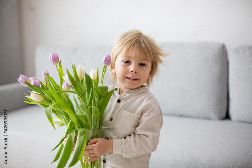 Beautiful blond boy, giving mother flowers and box with little gift for mothers day Beautiful blond boy, giving mother flowers and box with little gift for mothers day