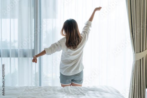 Fototapeta Naklejka Na Ścianę i Meble -  Back view of beautiful young Asian woman in white pajamas stretching after wake up in the morning in bedroom.