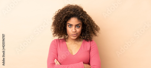 Young African American woman isolated on beige background with unhappy expression