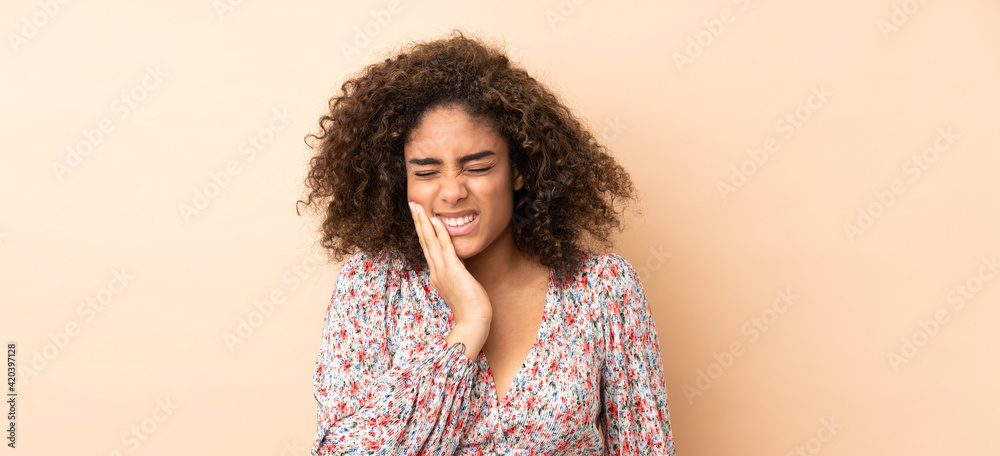 Young African American woman isolated on beige background with toothache
