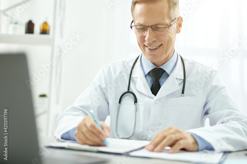 Cheerful doctor doing paperwork and using laptop in clinic
