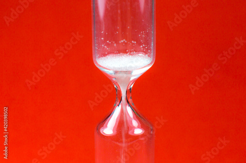 Sand clock on red background. Hourglass as time passing concept. Close up photo.