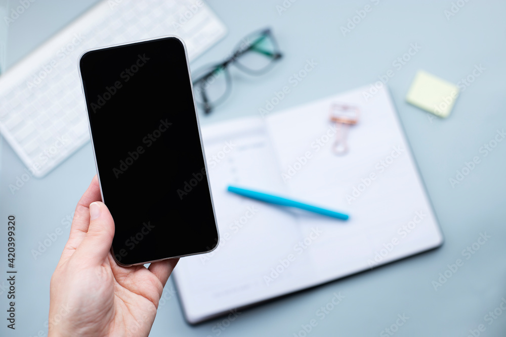 Smartphone in hand mock up over desktop with open planner and glasses. Planning, business mobile app concept Smartphone in hand mock up over desktop with open planner and glasses. Planning, business mobile app concept