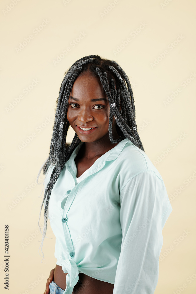 Portrait of young attractive Black woman with braided hair standing in light mint shirt against yellow background