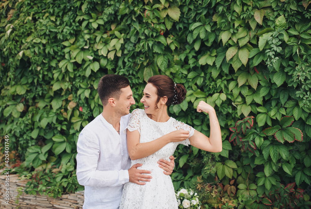 The merry newlyweds show their muscles and laugh. A stylish bride and cute bride smile and joke. Wedding portrait. The merry newlyweds show their muscles and laugh. A stylish bride and cute bride smile and joke. Wedding portrait.