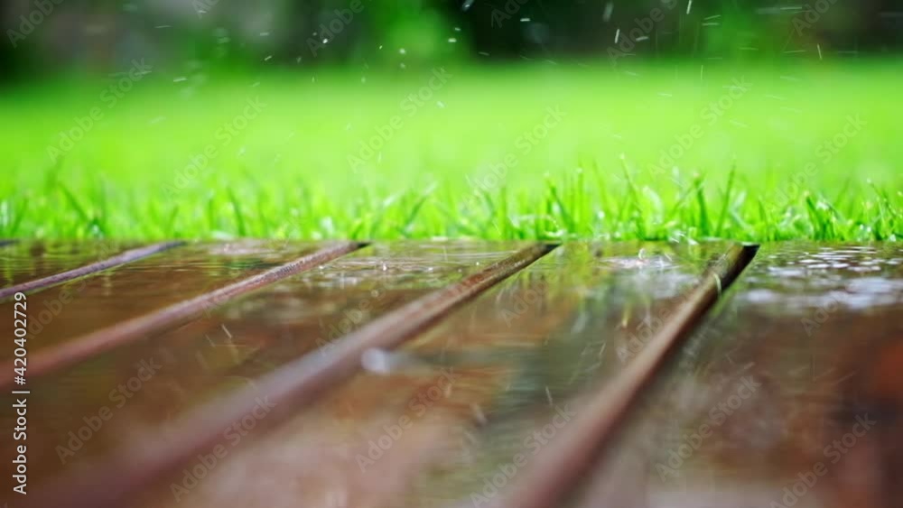 Rain falls on a wooden planks and green grass in the garden