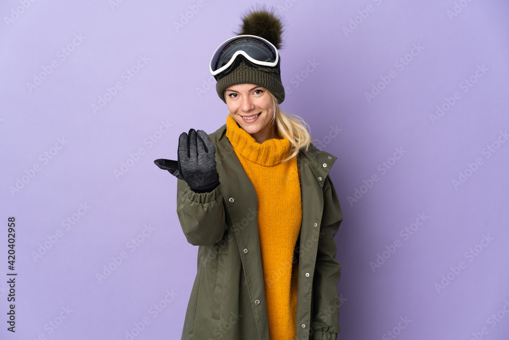 Skier Russian girl with snowboarding glasses isolated on purple background inviting to come with hand. Happy that you came Skier Russian girl with snowboarding glasses isolated on purple background inviting to come with hand. Happy that you came