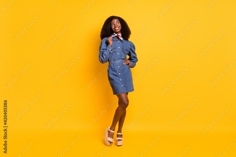 Full body photo of pretty dark skin girl look empty space arm touch play with scarf isolated on yellow color background Full body photo of pretty dark skin girl look empty space arm touch play with scarf isolated on yellow color background