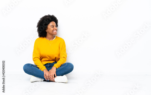 Young African American woman sitting on the floor looking side © luismolinero