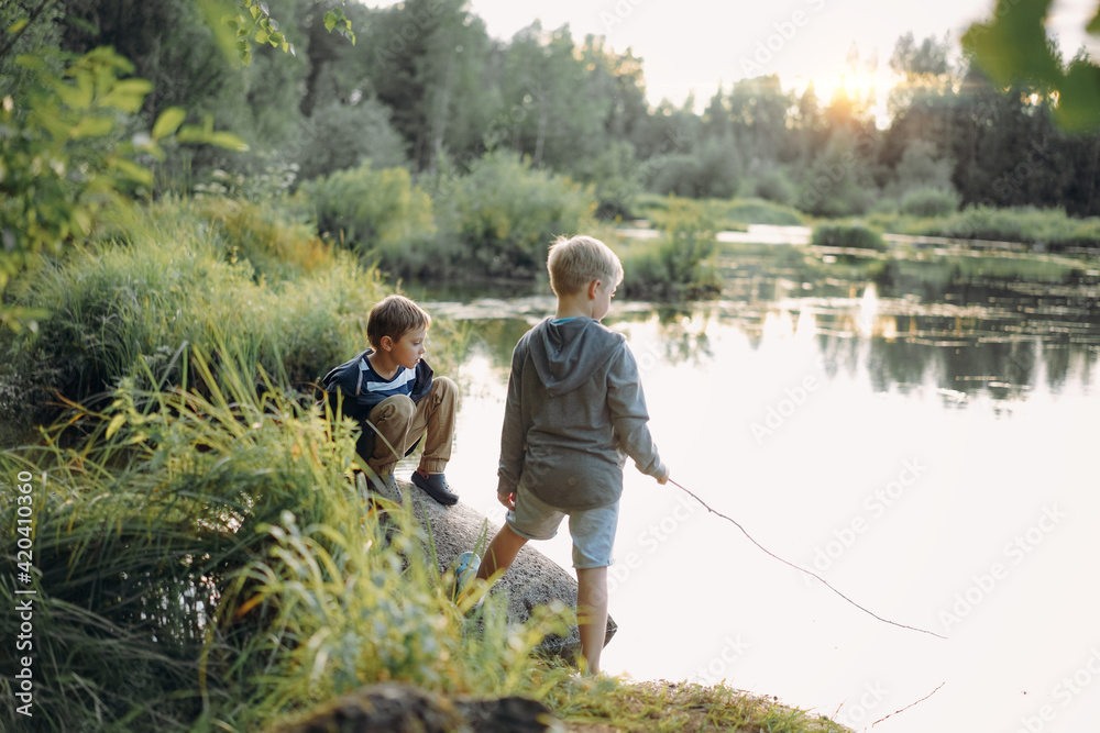 two caucasian boys pretending fishing on the pond. One is holding a cane imegine it is a rod. Image with slective focus and backlight two caucasian boys pretending fishing on the pond. One is holding a cane imegine it is a rod. Image with slective focus and backlight