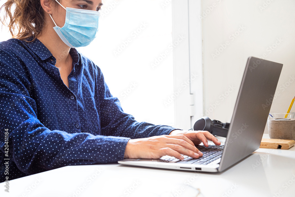 Naklejka premium woman with a mask working with her laptop in a bright office