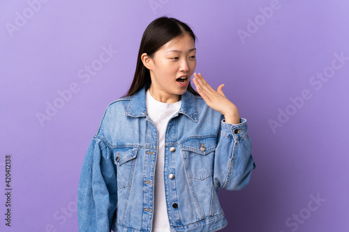 Young Chinese girl over isolated purple background yawning and covering wide open mouth with hand