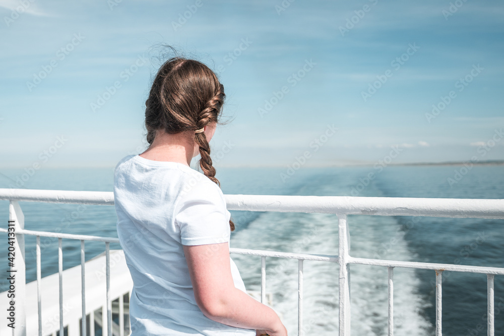 Young pretty girl in sunshine on ferry boat ship deck looking out to sea sailing away from harbour port blue summer skies over English Channel Calais to Dover England