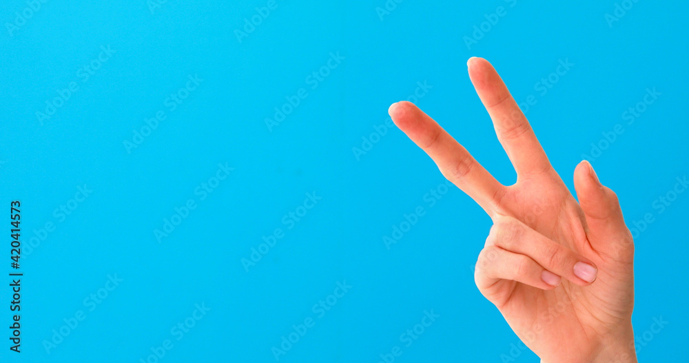Woman hand doing victory sign isolated on blue