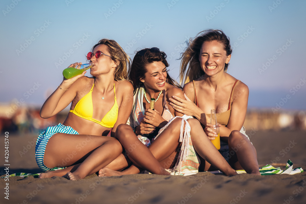 Happy young women sitting on the beach. Group of friends enjoying on beach holiday.