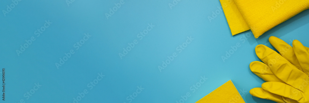 Yellow protective gloves, sponge and cloths on blue background. Top view of cleaning supplies. Banner. Copy space. Spring house cleaning concept.