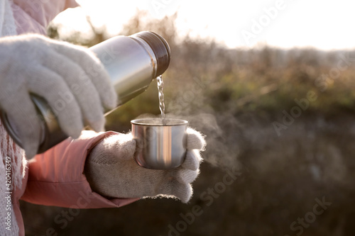 Woman pouring hot drink into cup from thermos outdoors, closeup