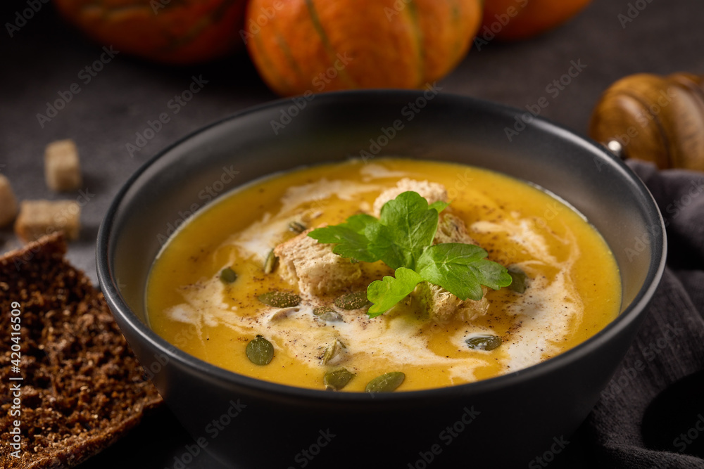 Pumpkin cream soup. Bowl with soup and orange pumpkins on gray background. Healthy, vegetarian food. Lenten menu Pumpkin cream soup. Bowl with soup and orange pumpkins on gray background. Healthy, vegetarian food. Lenten menu