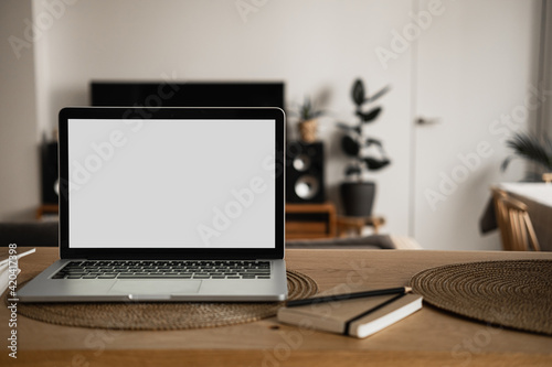 Laptop computer with blank screen, notebooks on wooden table in warm sunlight room. Aesthetic minimal interior design template with mockup copy space. Blog, web, social media concept.