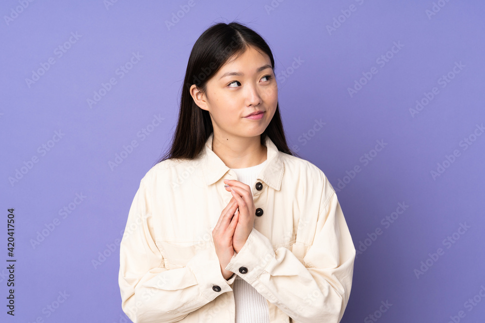 Young asian woman isolated on purple background scheming something