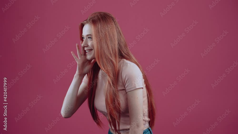 Young redhead with her hand on the cure, in profile, sideways to the left, in a pink casual T-shirt, isolated on a pink background. The concept of people's lifestyle. She screams and shouts to get Young redhead with her hand on the cure, in profile, sideways to the left, in a pink casual T-shirt, isolated on a pink background. The concept of people's lifestyle. She screams and shouts to get