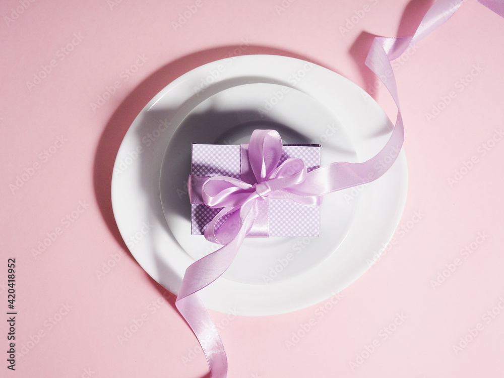 A gift box with a lilac ribbon lies on the plates saucers