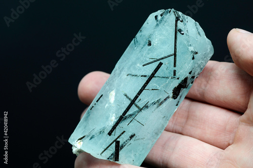 Fotografie Natural blue aquamarine huge hexagonal raw rough translucent crystal with black tourmaline crystals contemination inside the stone massive