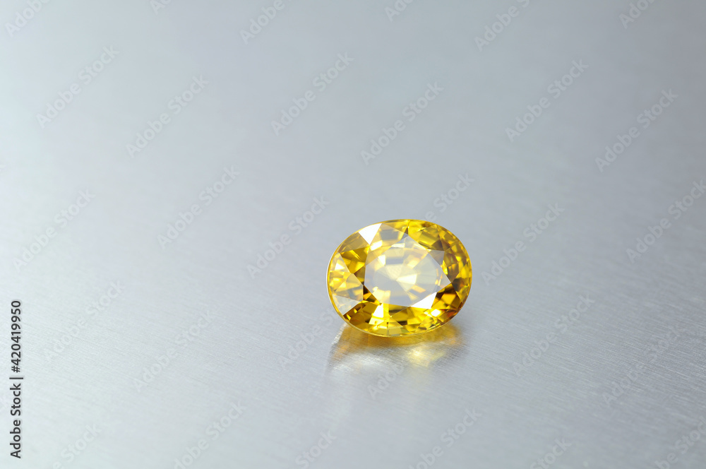 Natural clean free from inclusions bright yellow loose oval faceted zircon gemstone on light blue gray gradient aluminium metal background Natural clean free from inclusions bright yellow loose oval faceted zircon gemstone on light blue gray gradient aluminium metal background