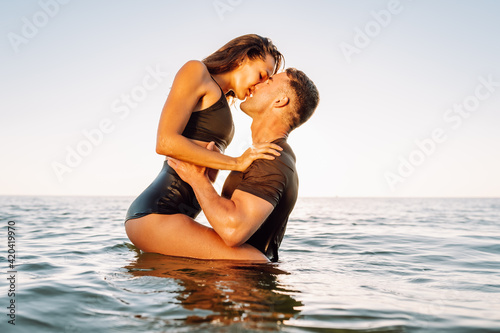 фотографія Happy young fit couple embrace each other with love in the sea or ocean at summer sunset